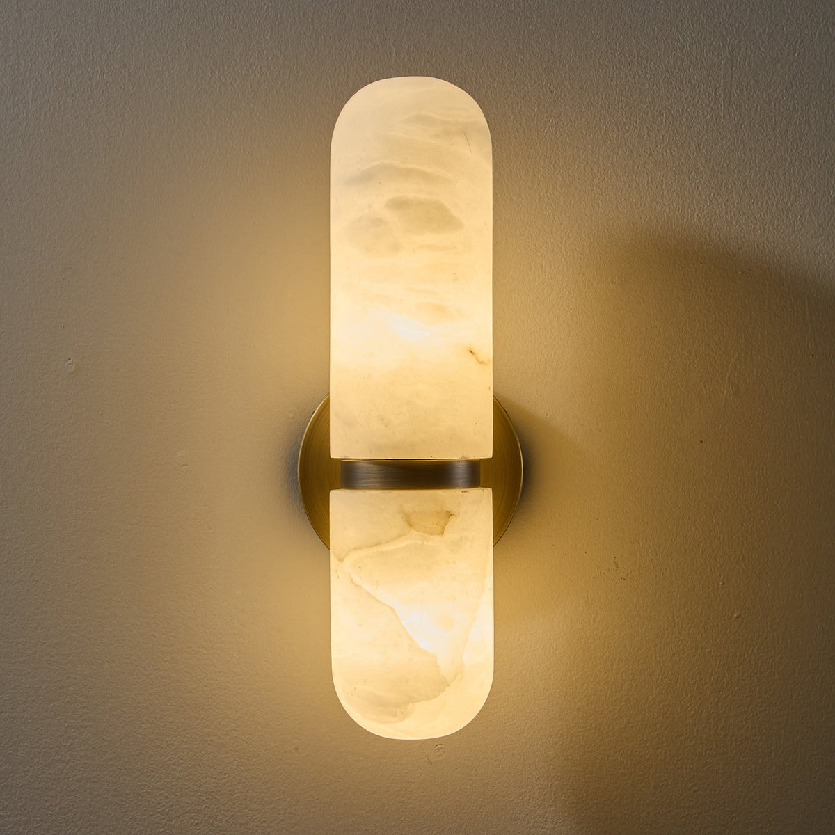 Close view of the lit Clérachic alabaster wall light, with golden veins showing in the glowing stone around the brass band.
