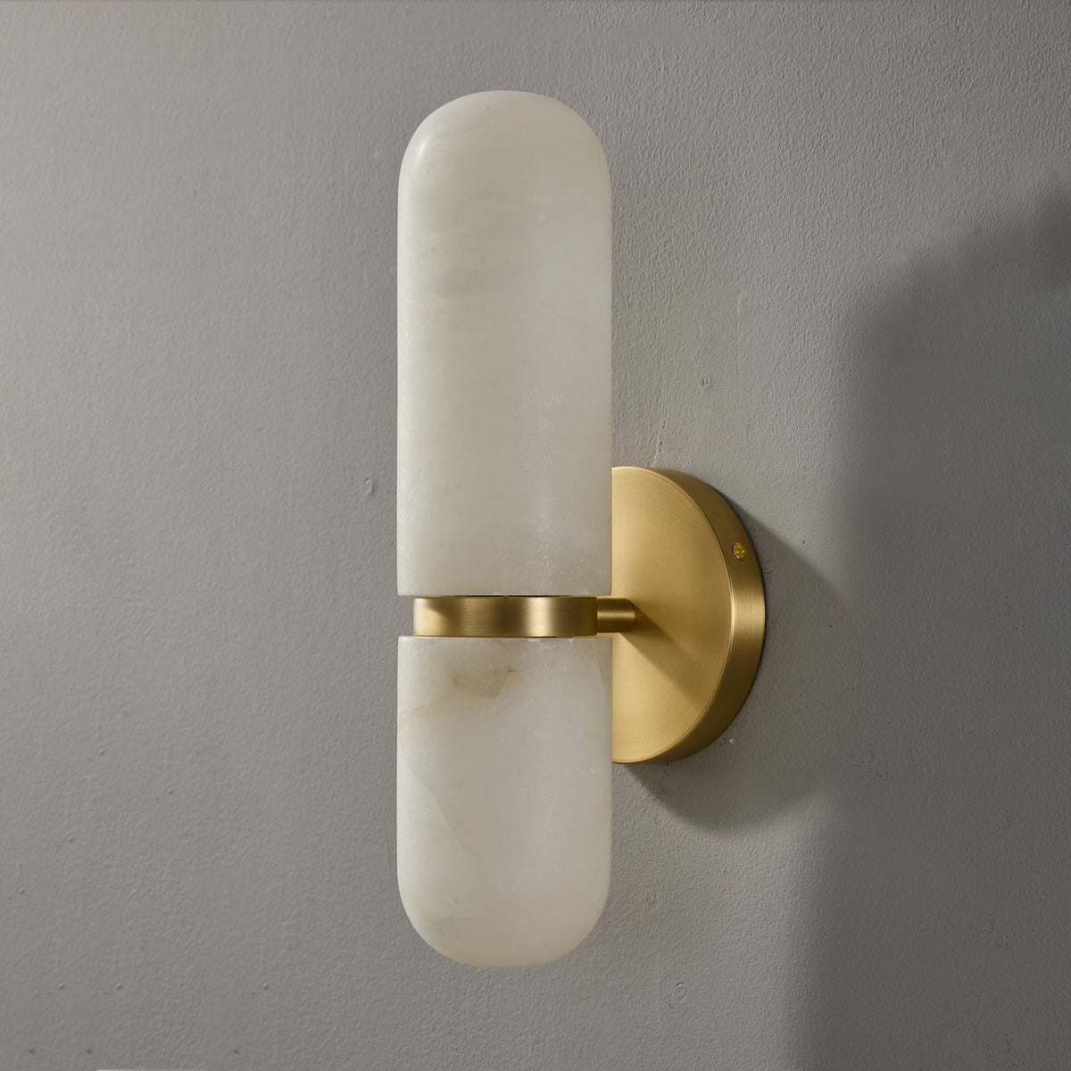 Side view of the Clérachic alabaster wall light on a grey wall, showing the stone shade standing off its round brass backplate.