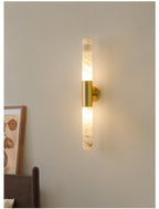 A lit Clérachic alabaster wall sconce with a gold-and-white finish, glowing up and down a taupe wall beside a framed print.