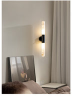 A black-and-white Clérachic wall light glowing beside a sheer curtain, above a leaning mirror and a bedside surface.