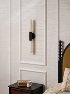 Unlit Clérachic wall light with a black centre band and white alabaster ends, mounted on a panelled wall above a bedside table.