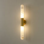 Close-up of the veined alabaster and the brass centre band of a lit Clérachic wall light on a grey-green wall.