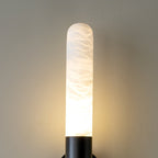 Close view of one lit alabaster tube of this Clérachic wall light, with a black collar and warm light at its base.