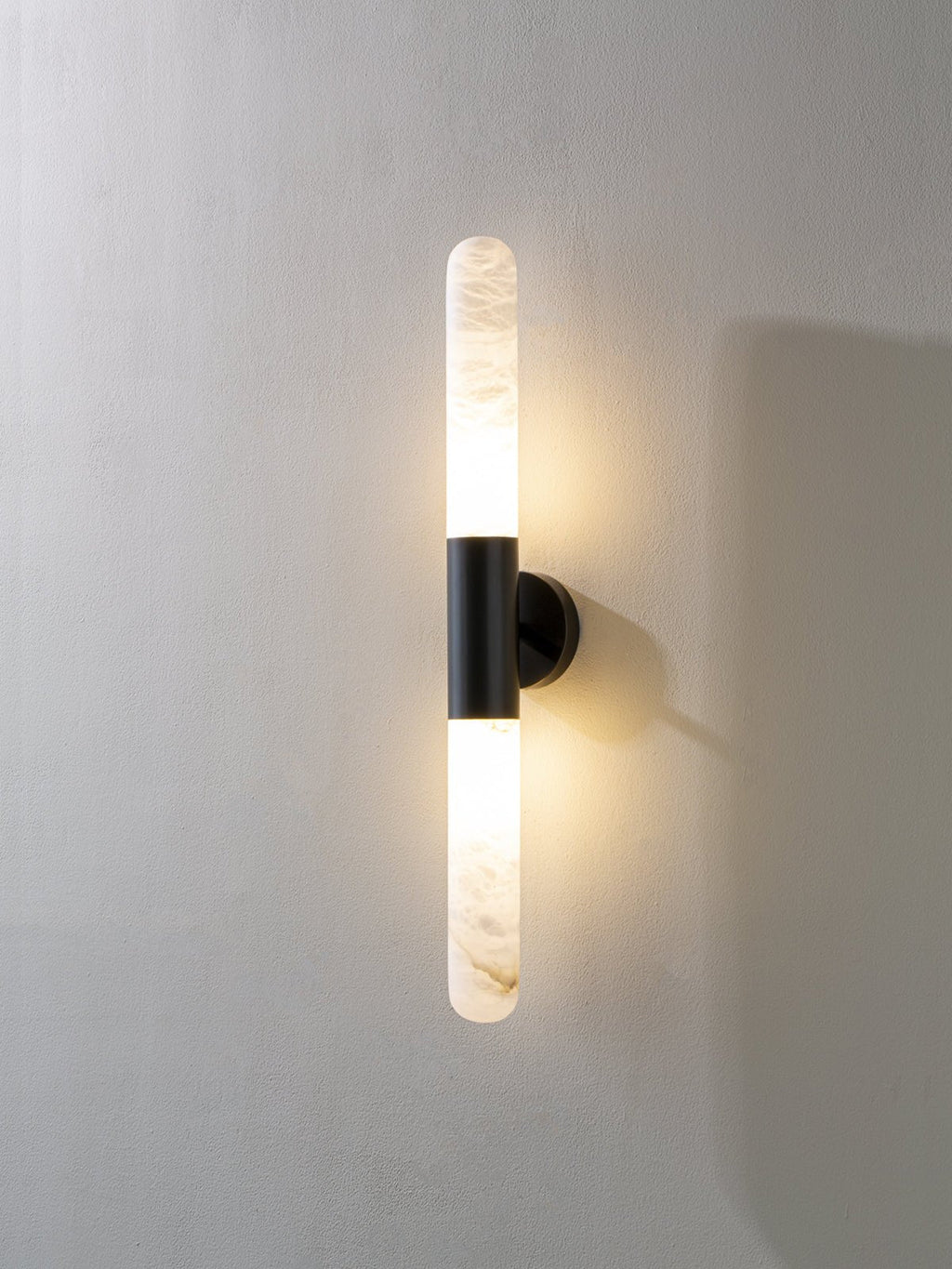 Another lit view of this Clérachic black-and-white wall light on a pale wall, with a narrower alabaster tube above and below the band.
