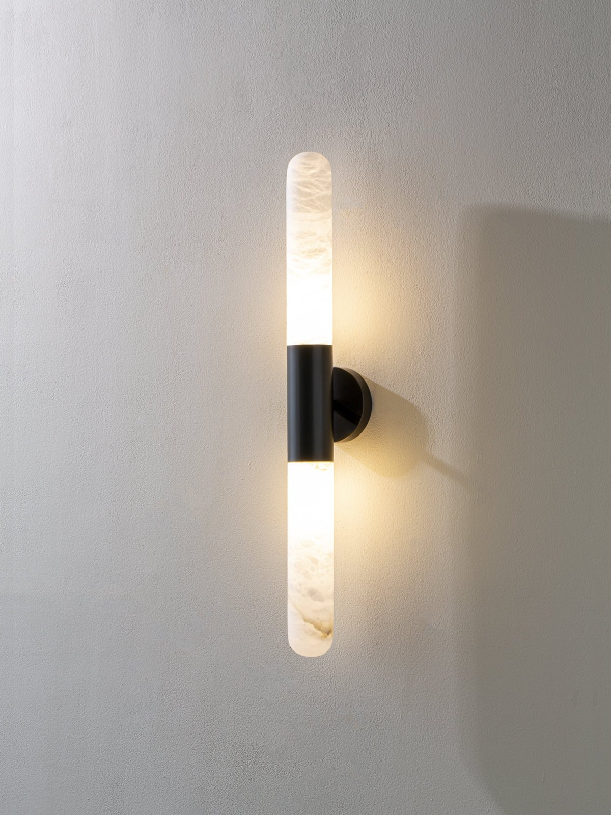 Another lit view of this Clérachic black-and-white wall light on a pale wall, with a narrower alabaster tube above and below the band.