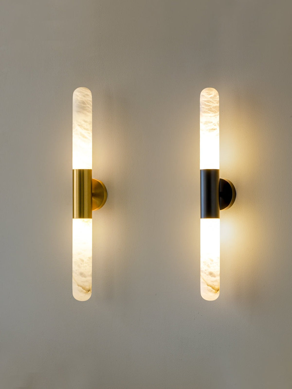The two Clérachic finishes, gold-and-white and black-and-white, hung side by side and lit, with a slim alabaster tube on each.