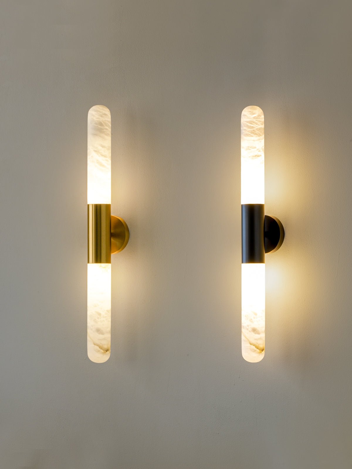 The two Clérachic finishes, gold-and-white and black-and-white, hung side by side and lit, with a slim alabaster tube on each.
