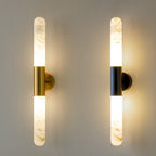 Close view of a pair of Clérachic wall lights, one gold and one black, both lit against a warm grey wall.