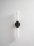 Unlit Clérachic wall light with a black band and white tube, against a plain white backdrop and soft shadow.