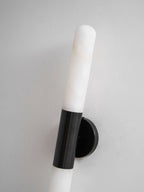 Close view of the black metal band and wall plate of this Clérachic wall light, with a white alabaster tube above it, on a grey wall.