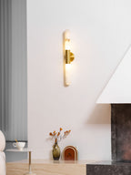 A lit Clérachic wall sconce with a brass band, above a low console with a vase, a small side table and a stone fireplace.