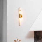 Glowing Clérachic gold-and-white wall light on a white wall, with the warm light rising and falling above a vase and a fireplace.