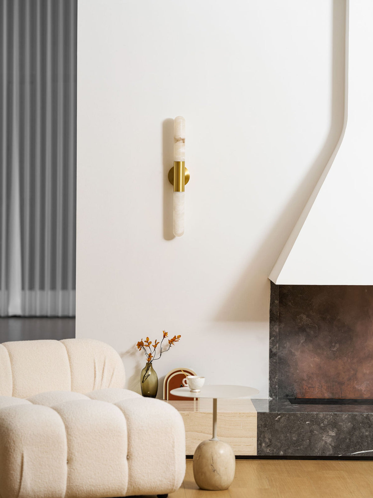 This Clérachic wall light hangs low and unlit above a cream boucle sofa and a round side table, with a stone fireplace on the right.