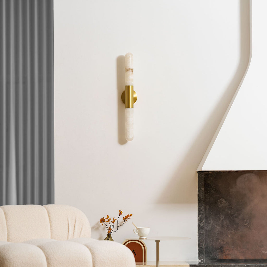 An unlit Clérachic wall light with a brass band, hung on a white wall near a boucle sofa, a vase of stems and a tray-style side table.