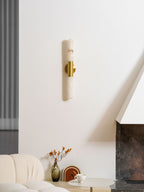 Narrow view of an unlit Clérachic gold-and-white wall sconce on a white wall, with a vase of orange stems and a boucle sofa below.