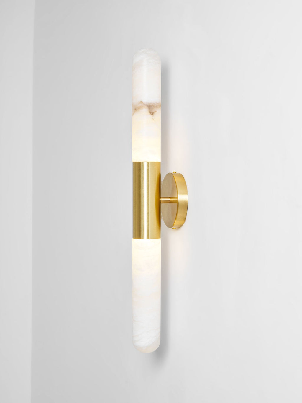 Gold-and-white Clérachic wall light cut out against a pale grey wall, with the brass band and round plate seen from a slight angle.