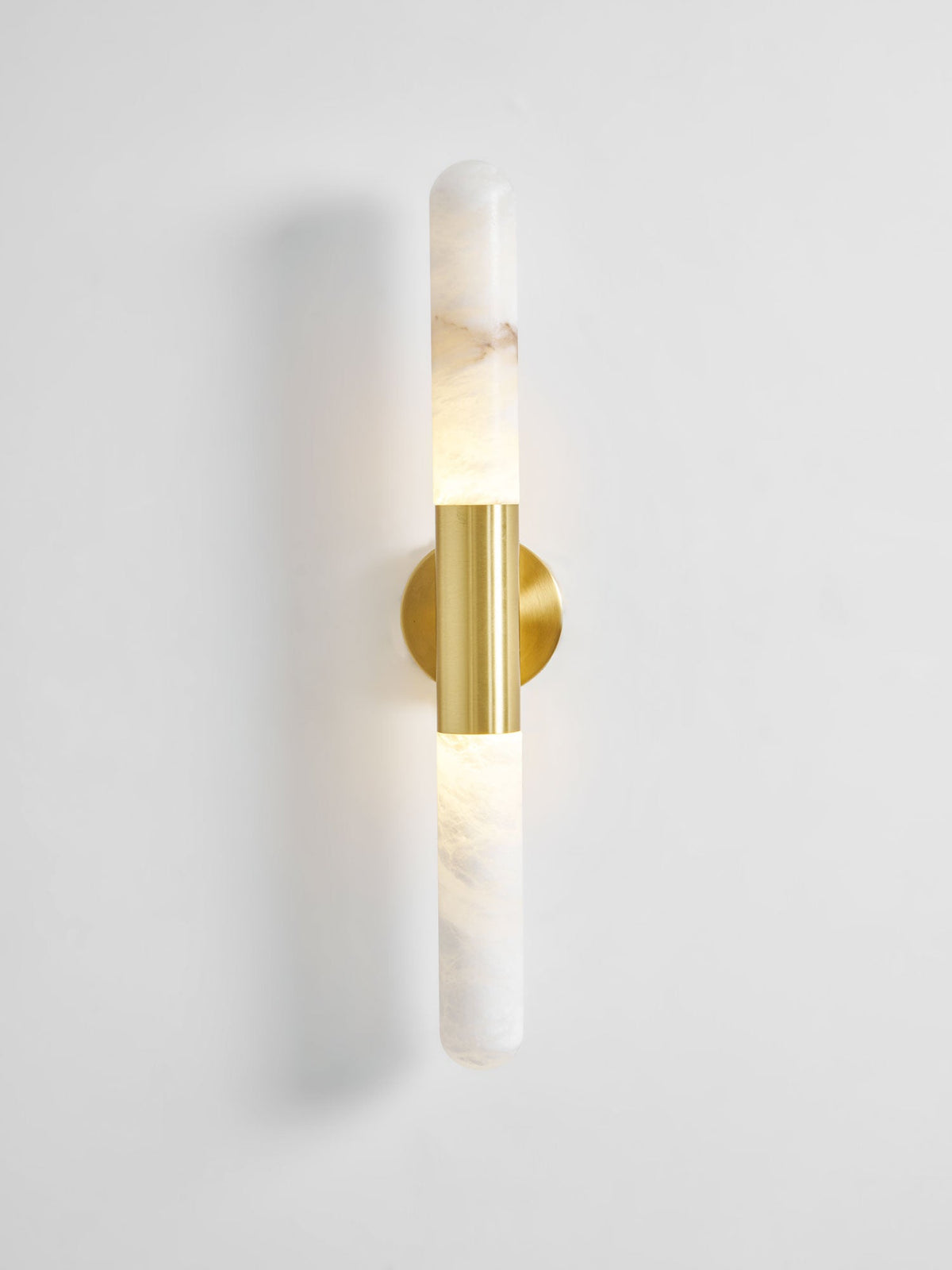 Lit Clérachic gold-and-white wall sconce on a pale wall, with a faint glow in the alabaster and a soft shadow to the left.