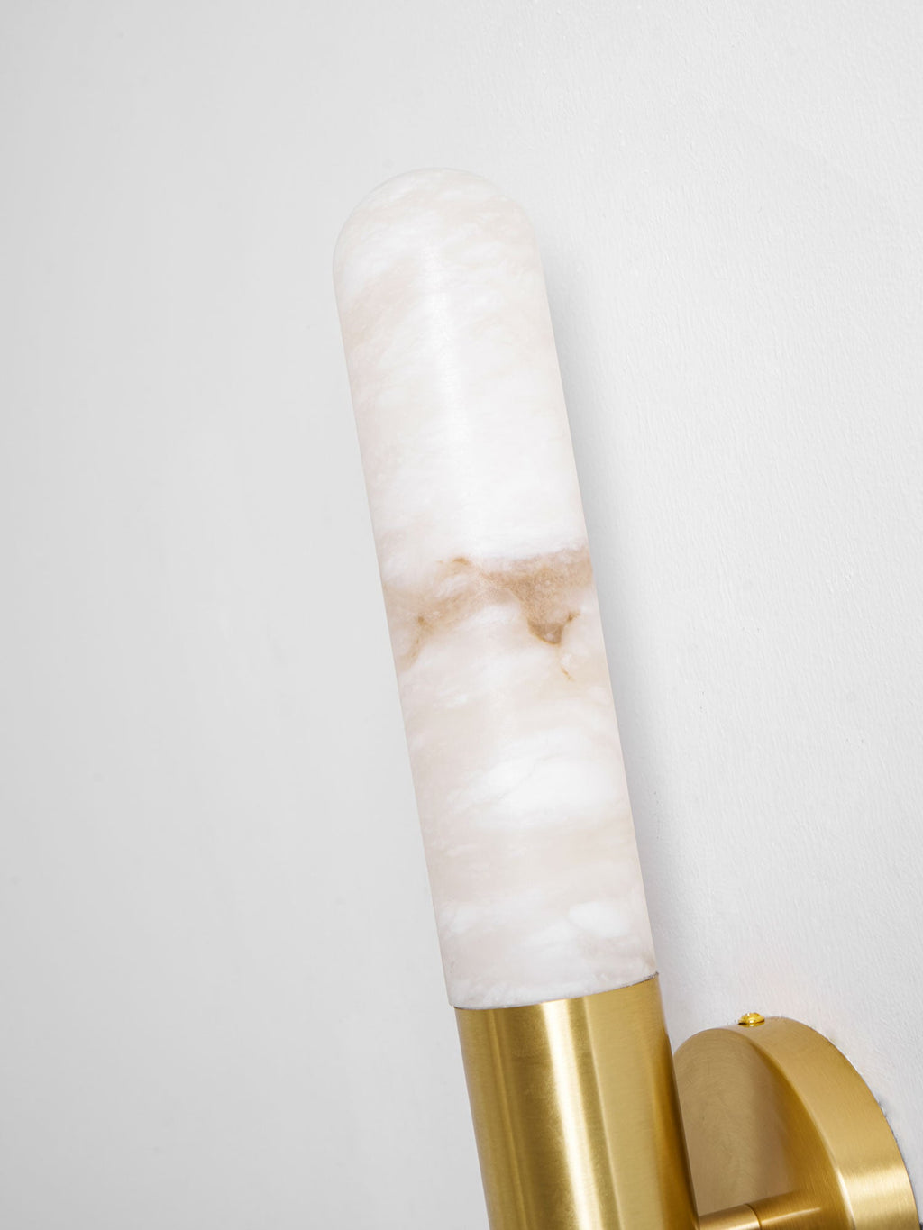Close view of the cloudy alabaster and the brass collar at the top of this Clérachic wall light, shown at an angle against a pale wall.