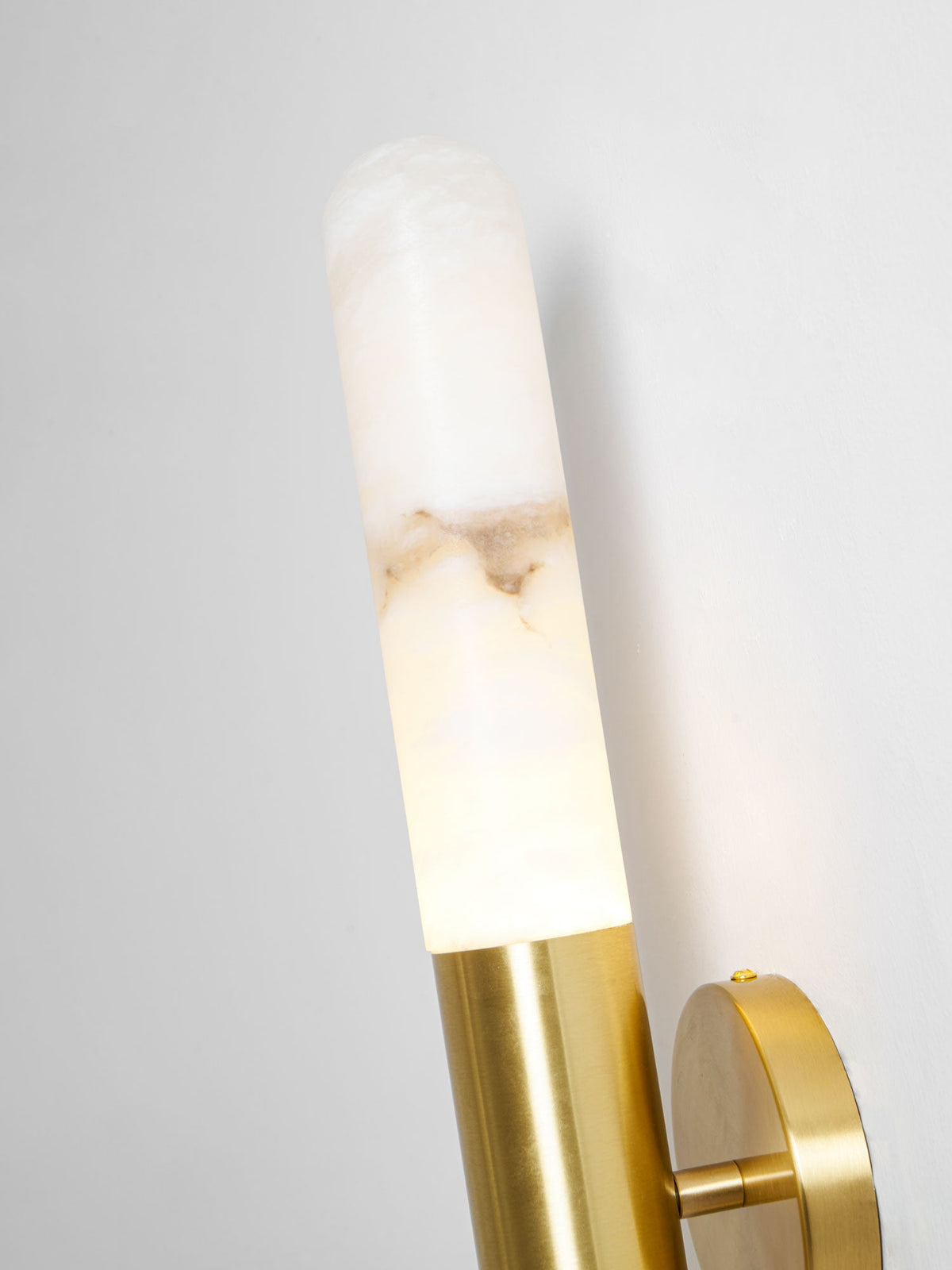Close view of a lit alabaster tube on this Clérachic wall light, glowing at the bottom where it meets the brass collar.