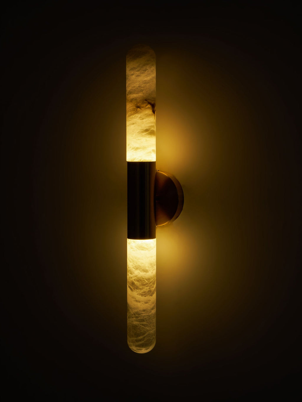 A Clérachic wall light with a dark band glowing amber against a black background, showing the alabaster veining lit from inside.