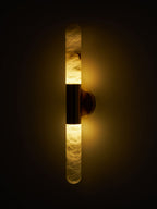 A Clérachic wall light with a dark band glowing amber against a black background, showing the alabaster veining lit from inside.
