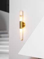 Lit Clérachic wall light with a brass band, close up on a white wall beside the sharp edge of a fireplace hood.