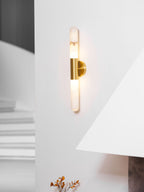 Clérachic gold-and-white wall sconce lit on a white wall, with the fireplace hood in the foreground and a soft sofa out of focus.