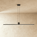 Clérachic matte black linear bar pendant, suspended on twin cables from a round ceiling canopy, glowing warm white along its length.