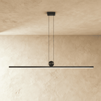 Clérachic matte black linear bar pendant, suspended on twin cables from a round ceiling canopy, glowing warm white along its length.