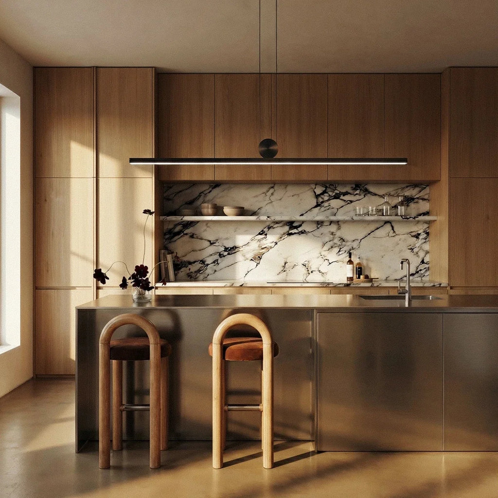 The Clérachic linear bar pendant hanging above a wood-cabinet kitchen island, warm white light spilling onto the marble backsplash.