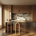 The Clérachic linear bar pendant hanging above a wood-cabinet kitchen island, warm white light spilling onto the marble backsplash.