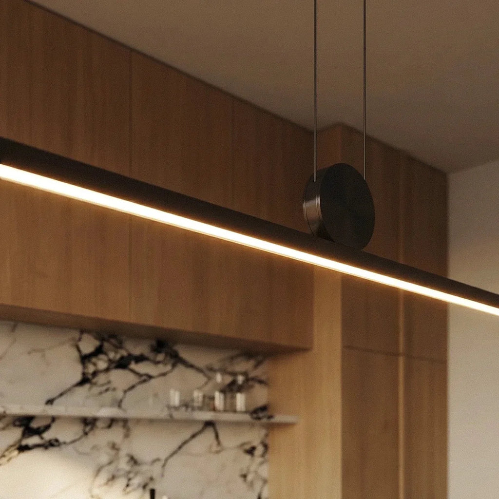 Close-up of the Clérachic pendant's round pivot disc and twin support cables, the aluminium bar glowing warm white below.