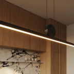 Close-up of the Clérachic pendant's round pivot disc and twin support cables, the aluminium bar glowing warm white below.