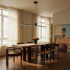 The Clérachic linear bar pendant centred above a dark wood dining table, its warm white glow lighting a bowl of oranges.