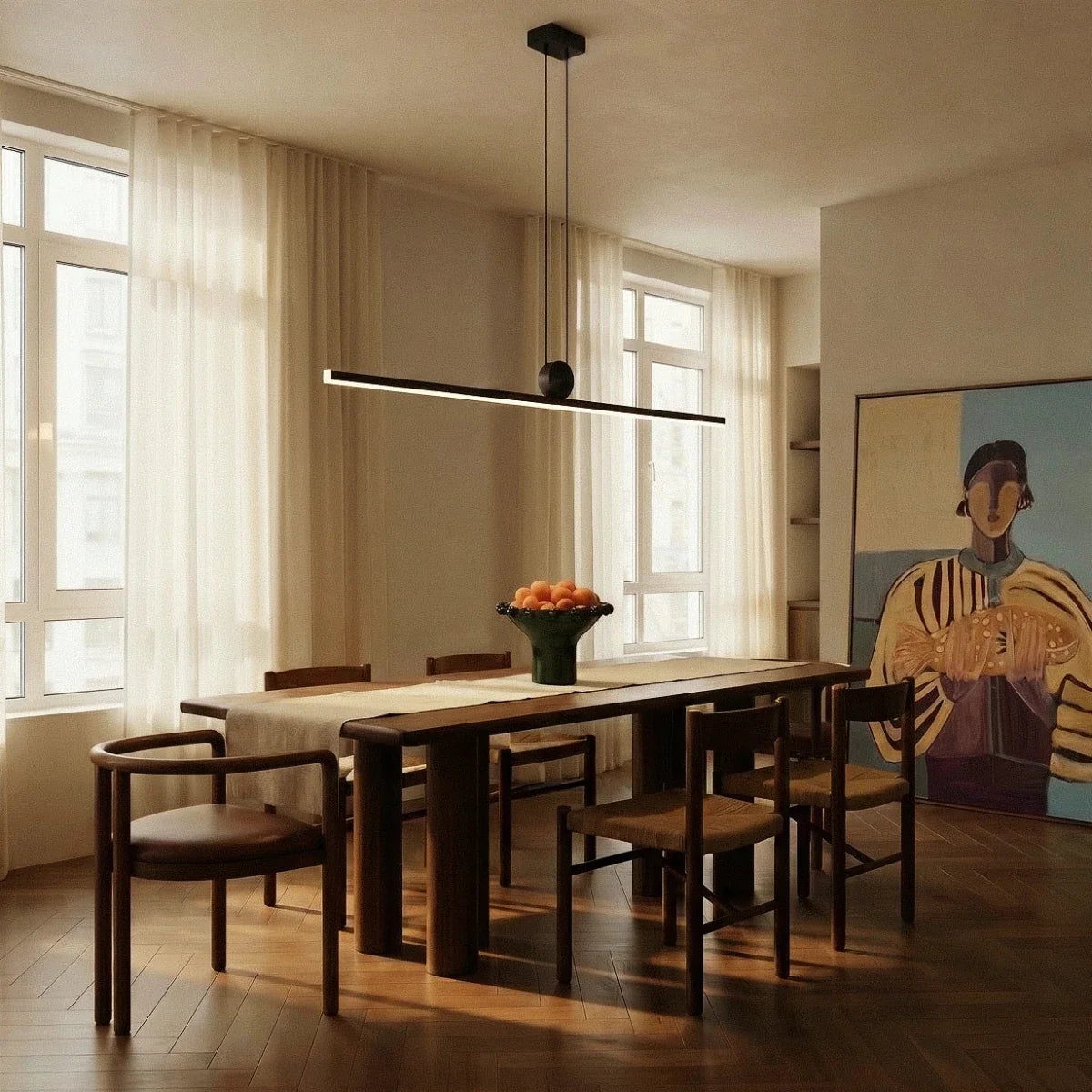 The Clérachic linear bar pendant centred above a dark wood dining table, its warm white glow lighting a bowl of oranges.