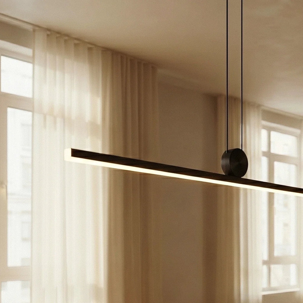 Close view of the Clérachic linear pendant light against sheer curtains, its aluminium bar glowing warm white by a window.