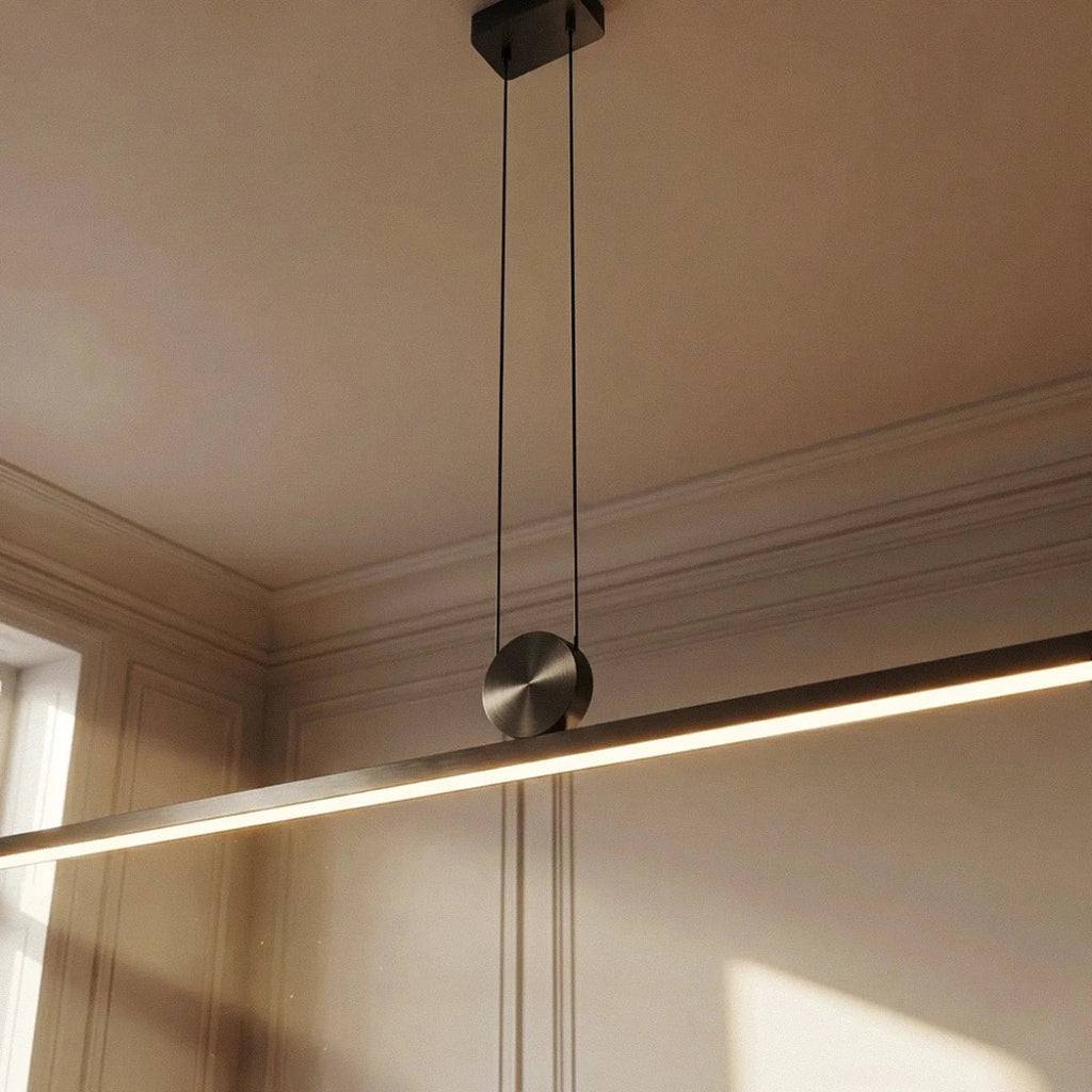 Close-up of the Clérachic pendant in a brushed metal finish, its round pivot disc and glowing bar set against panelled walls.