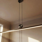 Close-up of the Clérachic pendant in a brushed metal finish, its round pivot disc and glowing bar set against panelled walls.