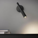 Black Clérachic wall light tilted toward the shelf below, its warm beam falling across the grey wall and a stack of books.