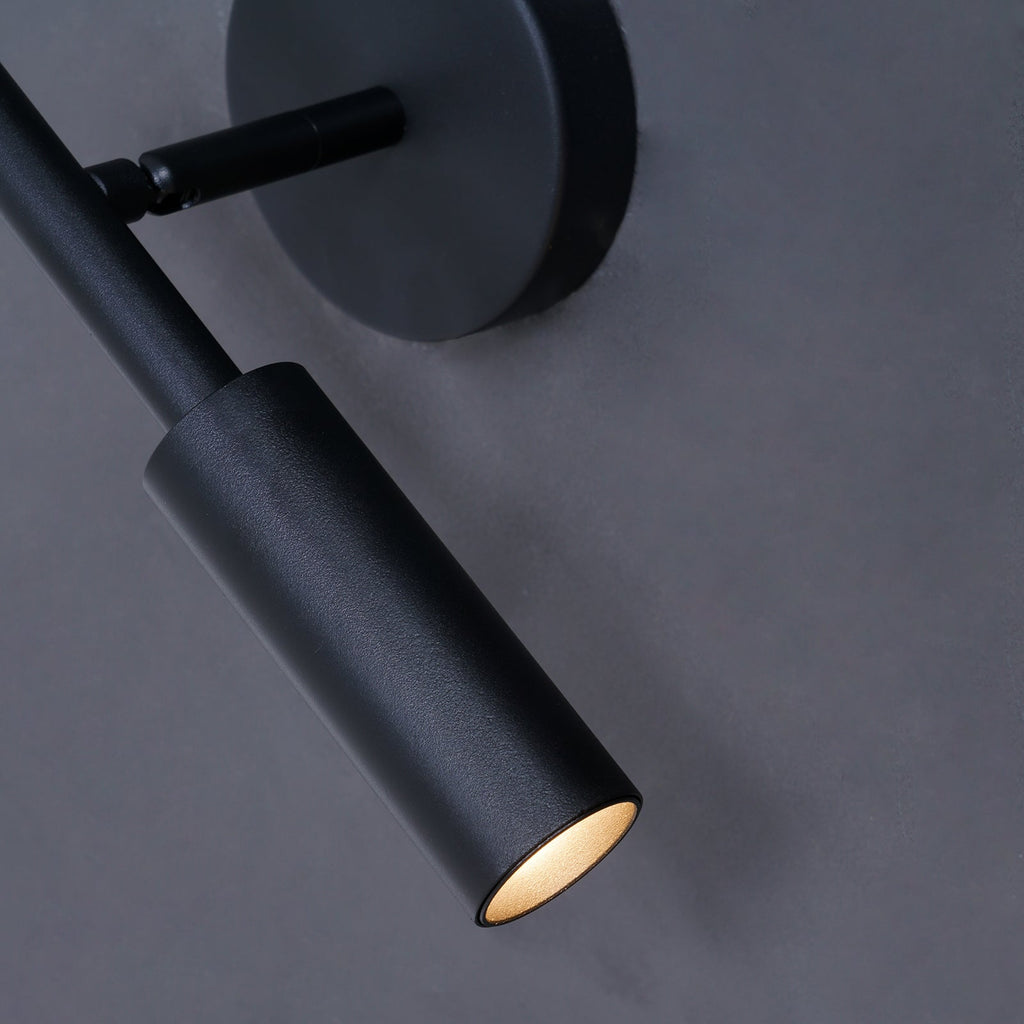 Close view of the matte black tube head and swivel joint of this Clérachic wall light, its warm light glowing at the tip.