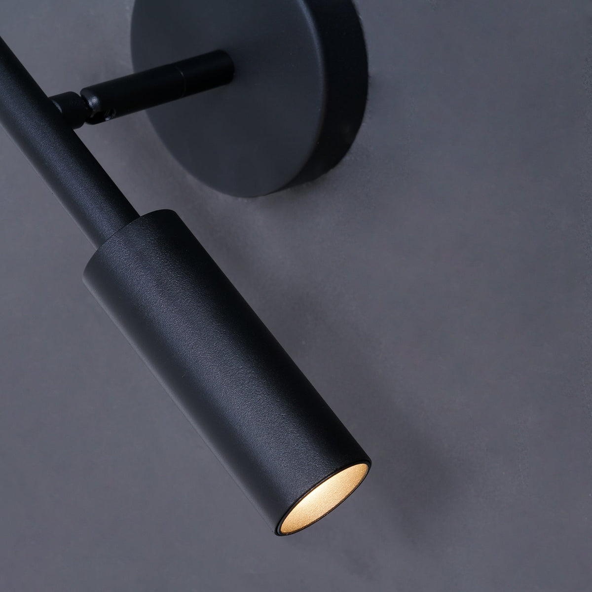 Close view of the matte black tube head and swivel joint of this Clérachic wall light, its warm light glowing at the tip.