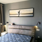 Two black Clérachic wall lights on either side of a leather headboard, below a framed sunset print on a grey wall.
