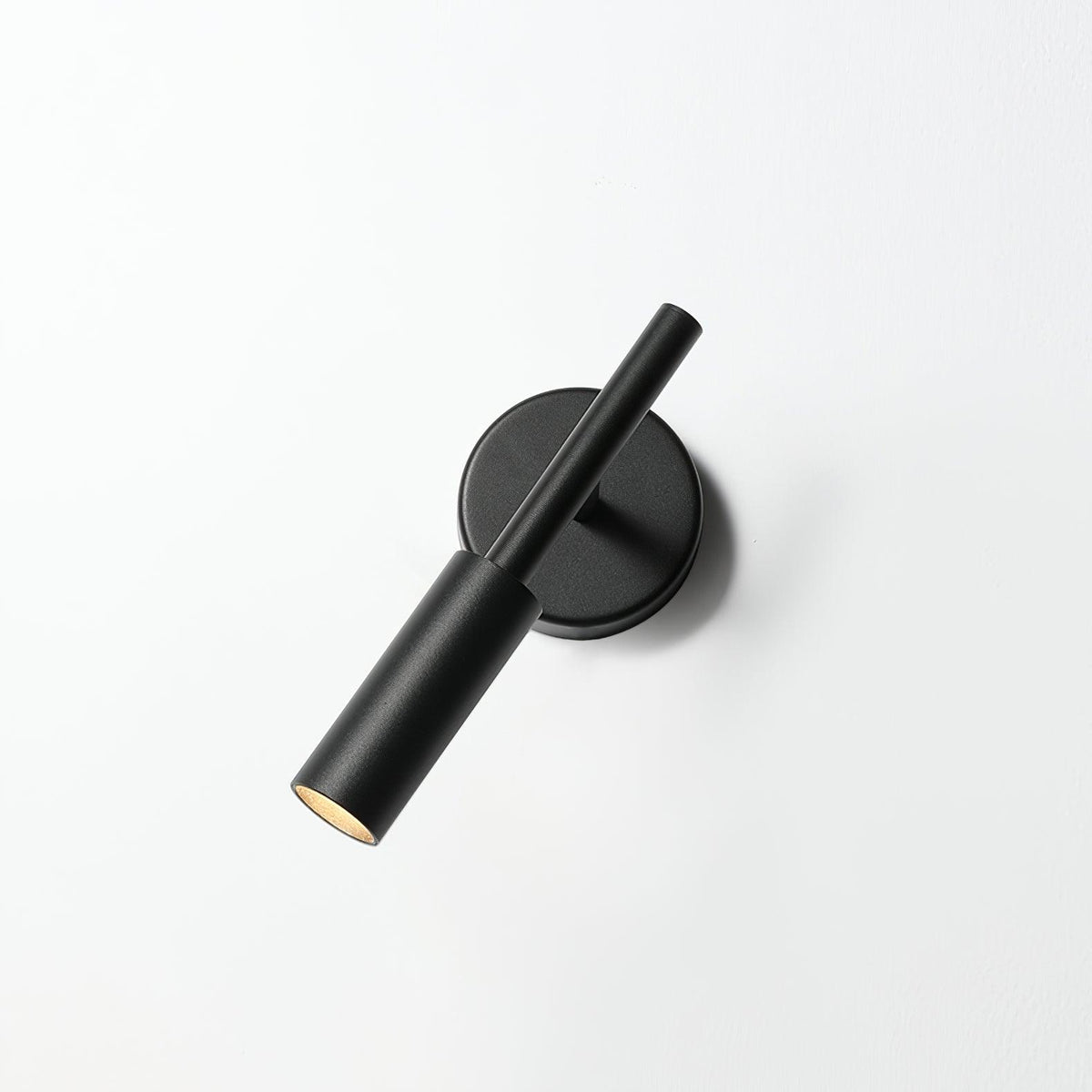 Black Clérachic wall light on a white wall with its tube head tilted across the backplate and the lit tip showing.