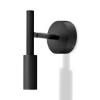 A black Clérachic wall light with a round backplate and a slim vertical tube head, with a faint reflection below it.