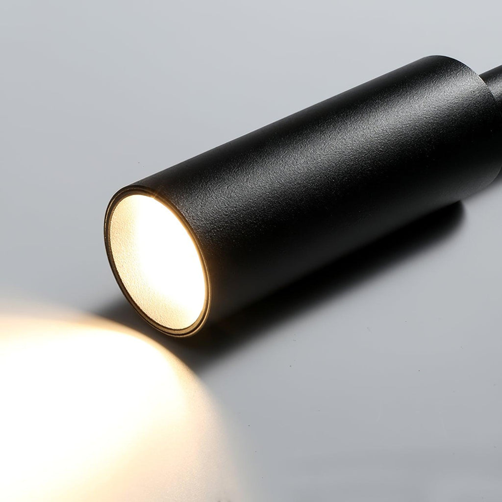 Close view of the lit end of the black tube head on this Clérachic wall light, with a warm beam spilling onto the surface.