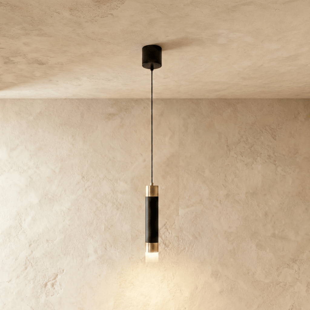 Clérachic single pendant light, a matte black cylinder with gold-tone caps and a frosted glowing base on a limewash wall.