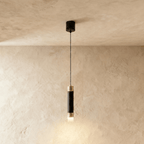 Clérachic single pendant light, a matte black cylinder with gold-tone caps and a frosted glowing base on a limewash wall.