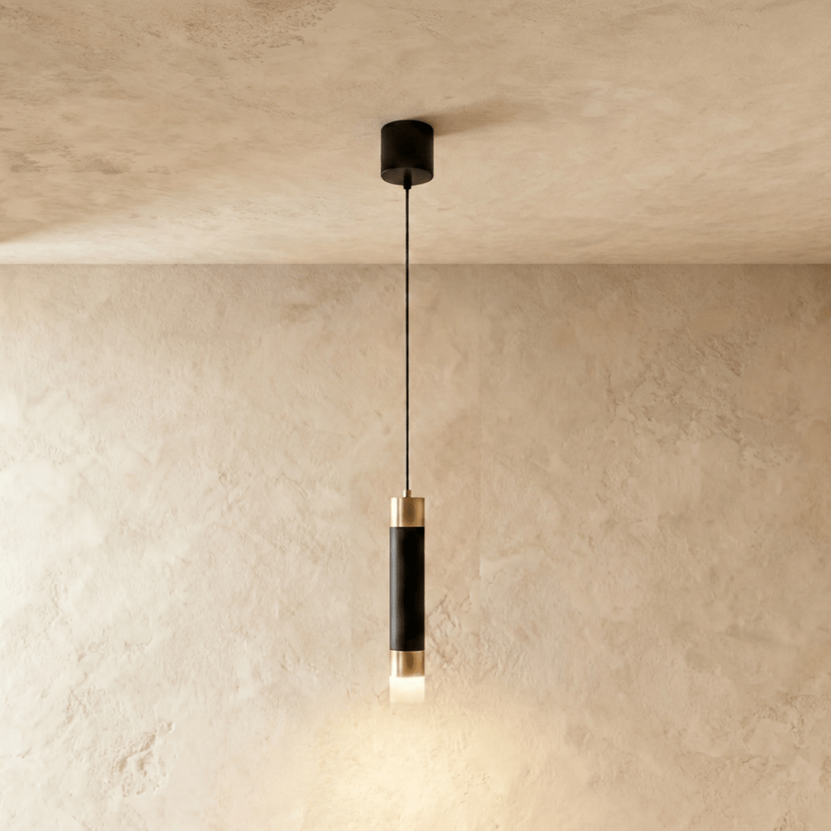 Clérachic single pendant light, a matte black cylinder with gold-tone caps and a frosted glowing base on a limewash wall.