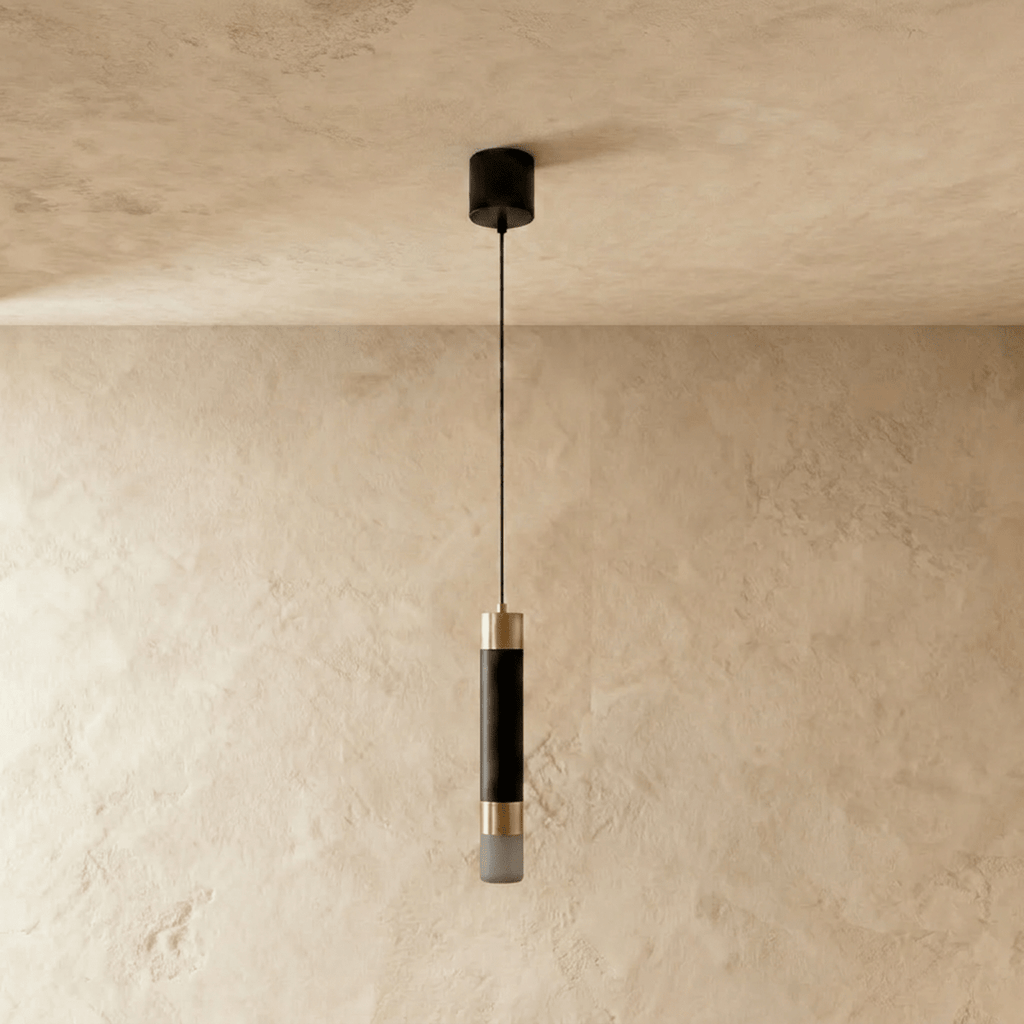 Clérachic single black cylinder pendant with gold-tone bands and a frosted end, switched off, on a limewash wall.