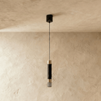 Clérachic single black cylinder pendant with gold-tone bands and a frosted end, switched off, on a limewash wall.